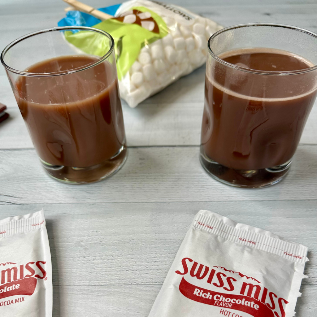 swiss miss hot chocolate packets, marshmallows, and two cups of hot chocolate